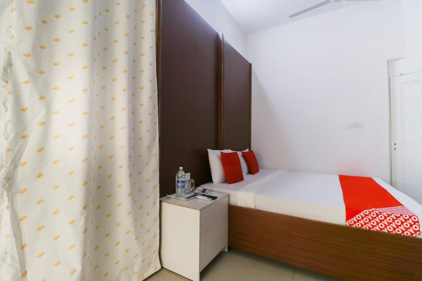 Guest room with tall wooden headboard, bedside table and curtained window